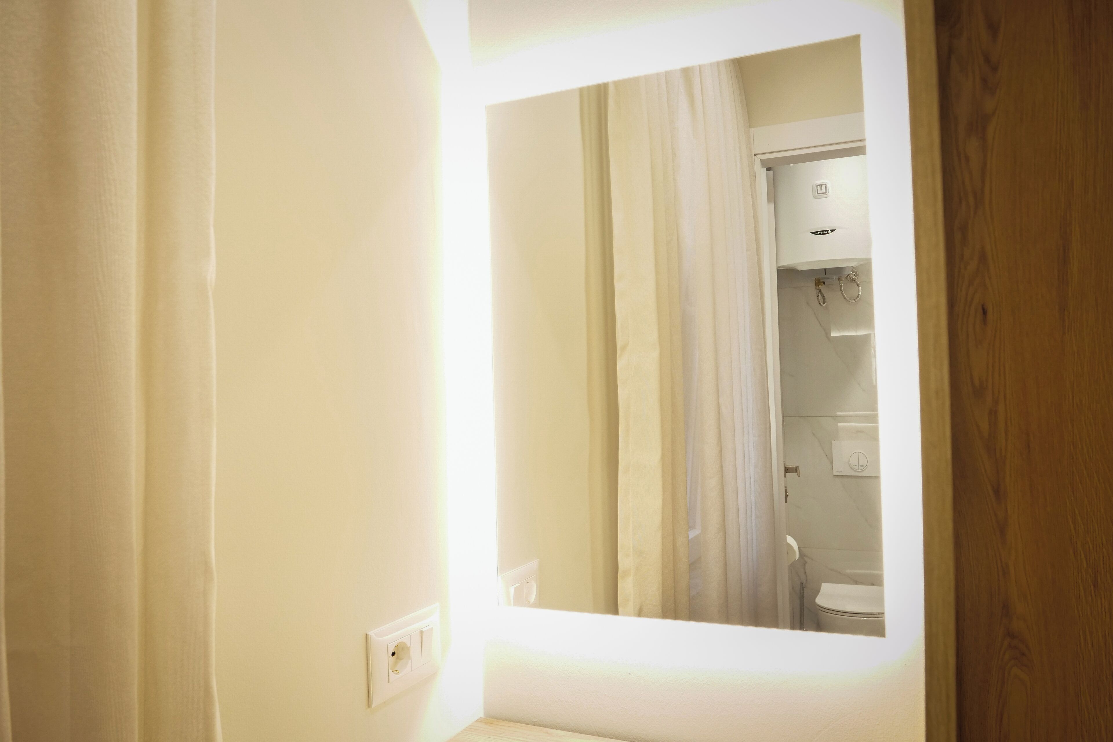 A bathroom with a white toilet, a shower area, and a mirror reflecting the room.