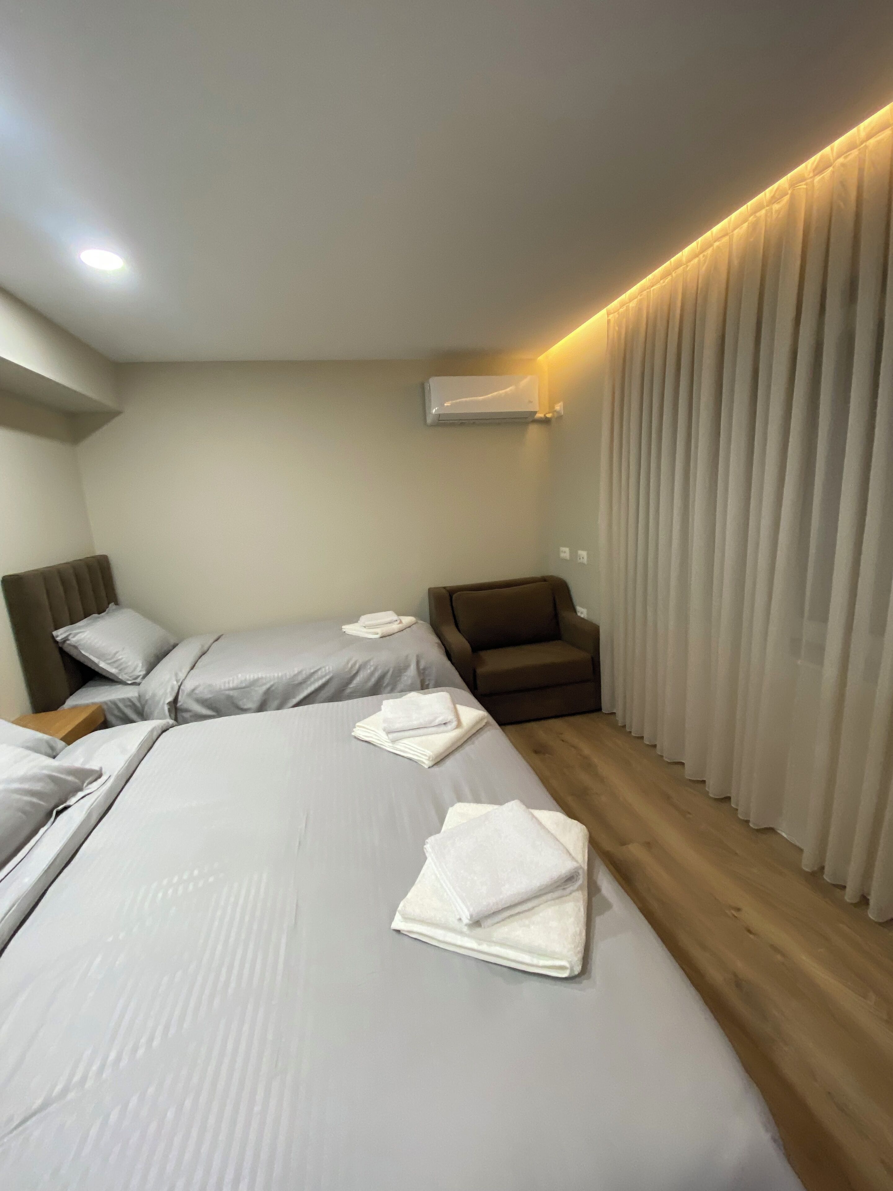 A hotel room with two beds, a chair, and a large window with curtains.
