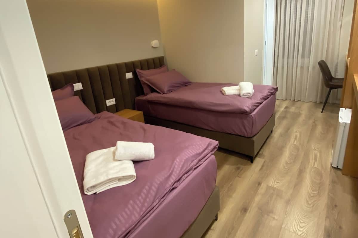 Een hotelkamer met twee bedden, een houten vloer en een raam met gordijnen.