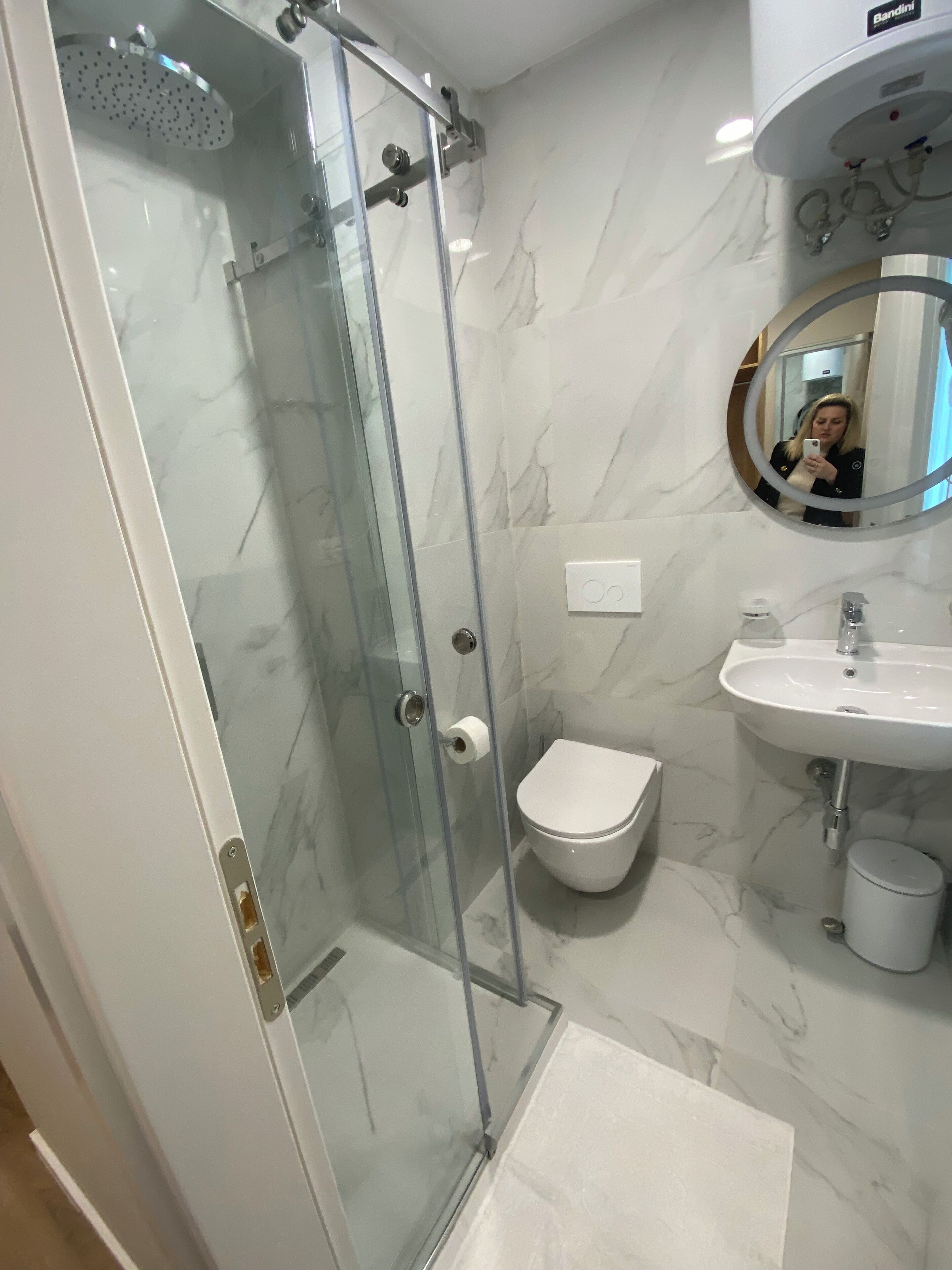 A modern bathroom with a glass-enclosed shower, a white toilet, and a sink with a mirror above it.