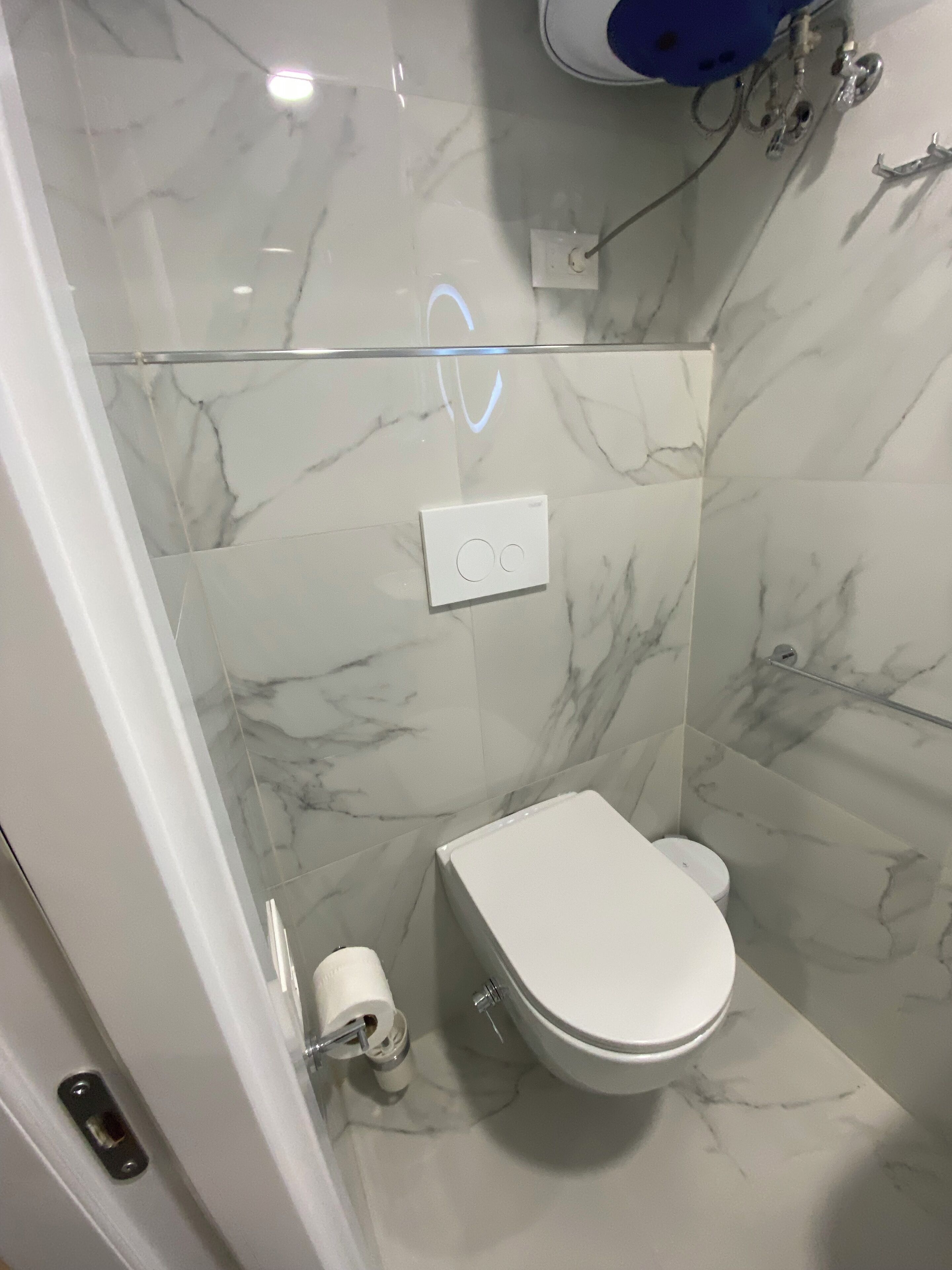 A bathroom with a toilet, marble walls, and a glass shower enclosure.