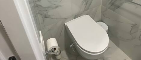 A bathroom with a toilet, marble walls, and a glass shower enclosure.