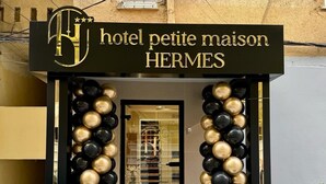 L’entrée de l’hôtel Petite Maison Hermès se distingue par sa façade noire et dorée, une porte en verre et un escalier menant à l’entrée.