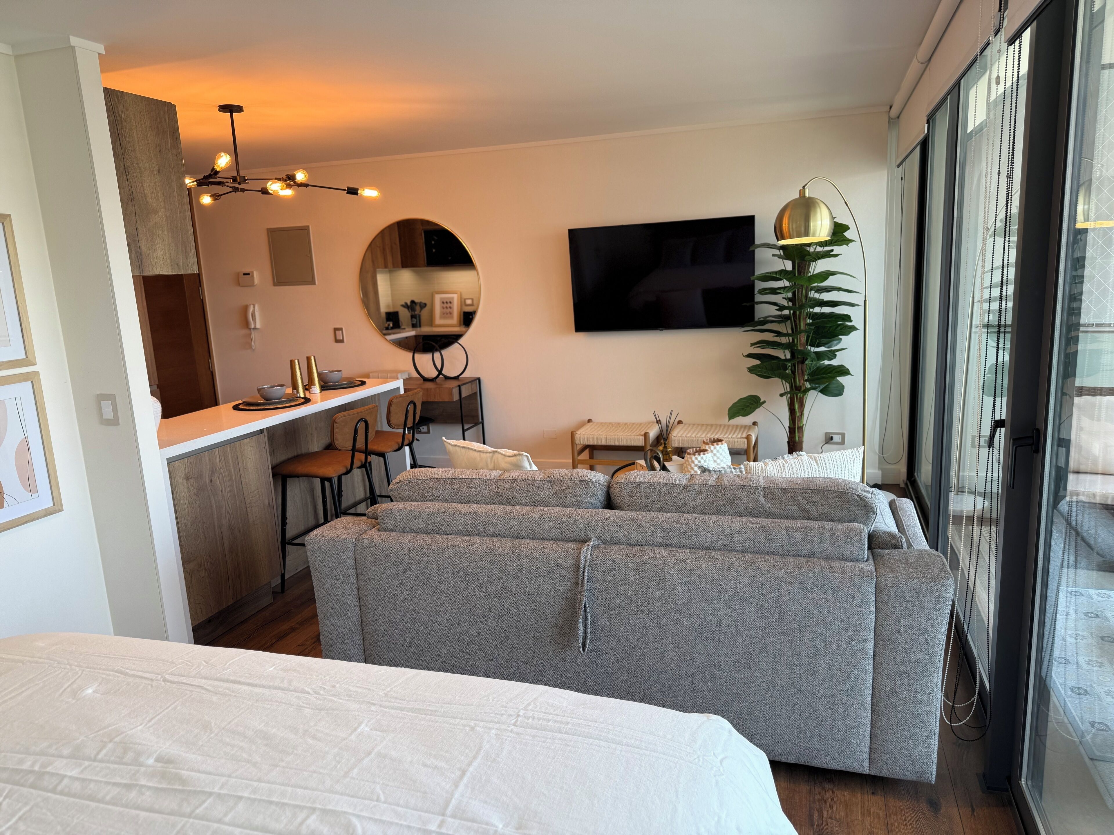 A modern hotel room with a sofa set, a dining area, a TV, and a large window.