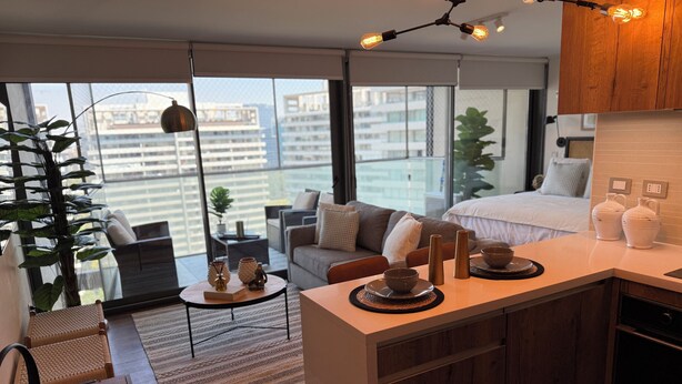 Un apartamento moderno con cocina, comedor y sala de estar con un amplio ventanal con vistas a un paisaje urbano.