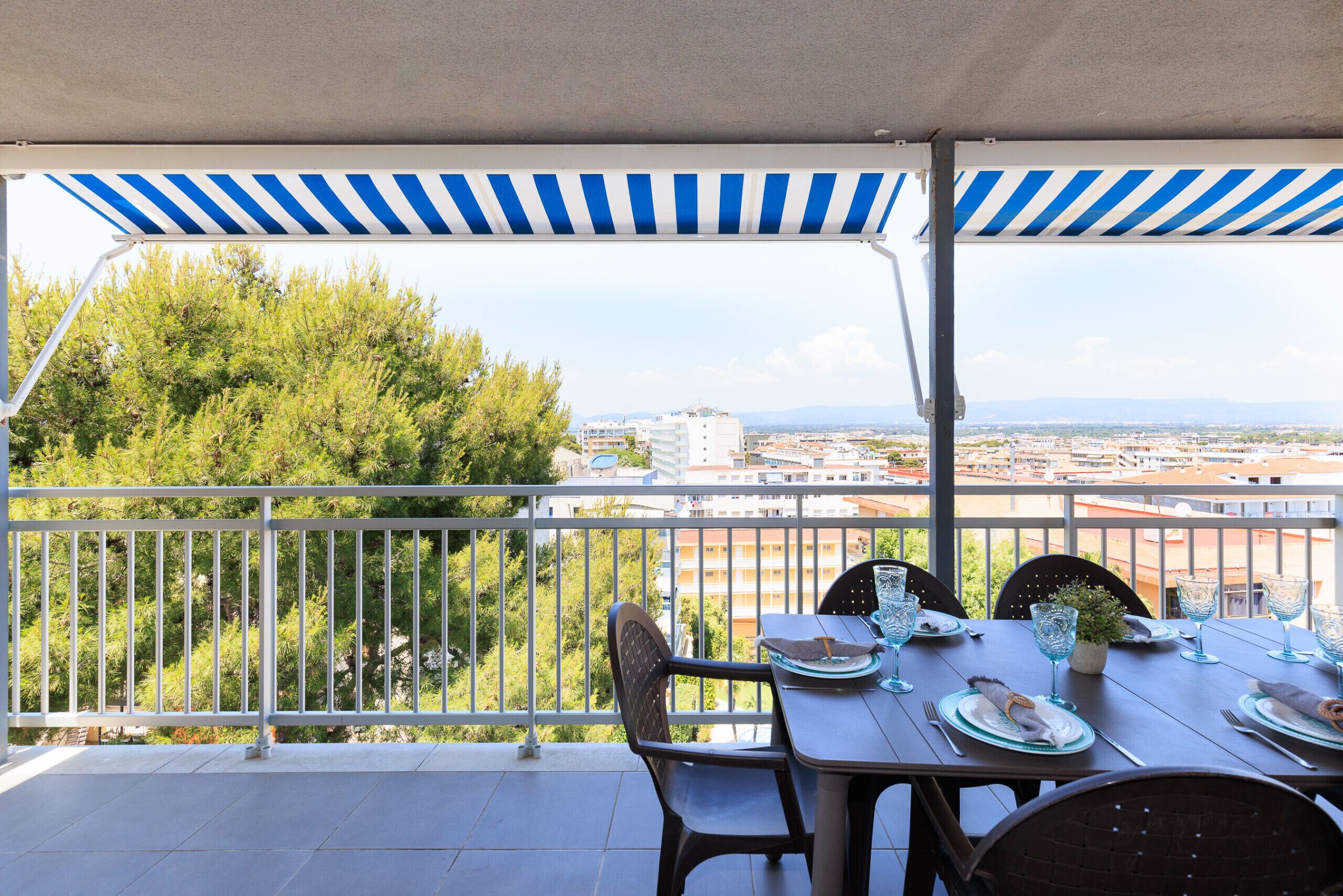 A balcony with a table set for dining, overlooking a cityscape with trees and buildings.
