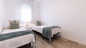 Ein Schlafzimmer mit zwei Betten, einem Nachttisch, einer Lampe und einem Fenster mit Jalousien.
