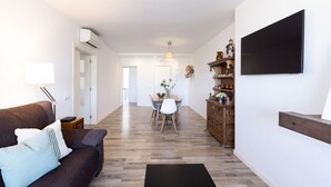 Ein Wohnzimmer mit einer Couch, einem Flachbildfernseher, einem Holzkabinett und einem Essbereich mit Tisch und Stühlen.