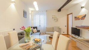 A modern living room with a glass dining table, two sofas, a TV, and a fireplace. - Volta Apartment by Rent all Como (Como)