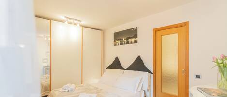 A bedroom with a bed, a nightstand, a door, and a wall-mounted picture.