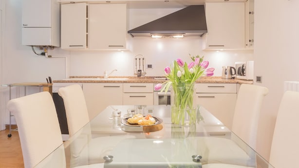 A modern kitchen with white cabinets, a glass dining table, and a vase of flowers. - Volta Apartment by Rent all Como (Como)