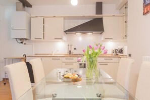 A modern kitchen with white cabinetry, a glass dining table, and a vase of flowers. - Volta Apartment by Rent all Como (Como)