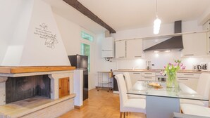 A modern kitchen with a built-in wood-burning stove, white cabinets, and a dining area with a glass table and white chairs. - Volta Apartment by Rent all Como (Como)