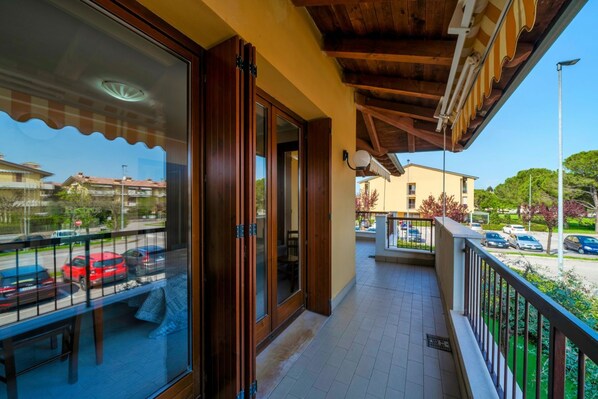 A balcony with a wooden ceiling, a glass door, and a view of parked cars and buildings.