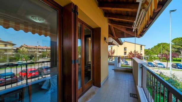 A balcony with a wooden ceiling, a glass door, and a view of parked cars and buildings. - Girasole Apartment - with air conditioning, garage and WiFi (Sirmione)