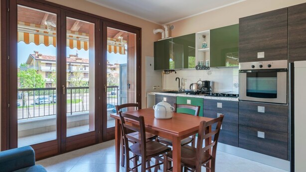 A modern kitchen with a dining area, a balcony with a view of buildings, and a sliding glass door. - Girasole Apartment - with air conditioning, garage and WiFi (Sirmione)