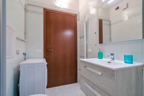 A bathroom with a wooden door, white tiles, a white sink with a mirror, and a towel rack. - Girasole Apartment - with air conditioning, garage and WiFi (Sirmione)