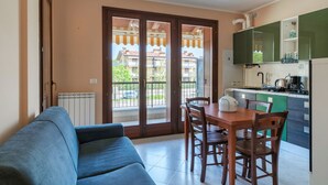 A living room with a blue sofa, a wooden dining table with chairs, a kitchen with green cabinets, and a sliding glass door leading to a balcony. - Girasole Apartment - with air conditioning, garage and WiFi (Sirmione)