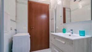 A bathroom with a wooden door, white tiles, a white sink with a mirror, and a towel rack. - Girasole Apartment - with air conditioning, garage and WiFi (Sirmione)