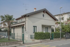 A two-story residential building with a balcony, a small garden, and a street view.
