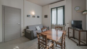 A compact living space with a dining table, chairs, a sofa, a TV on a stand, and a door.