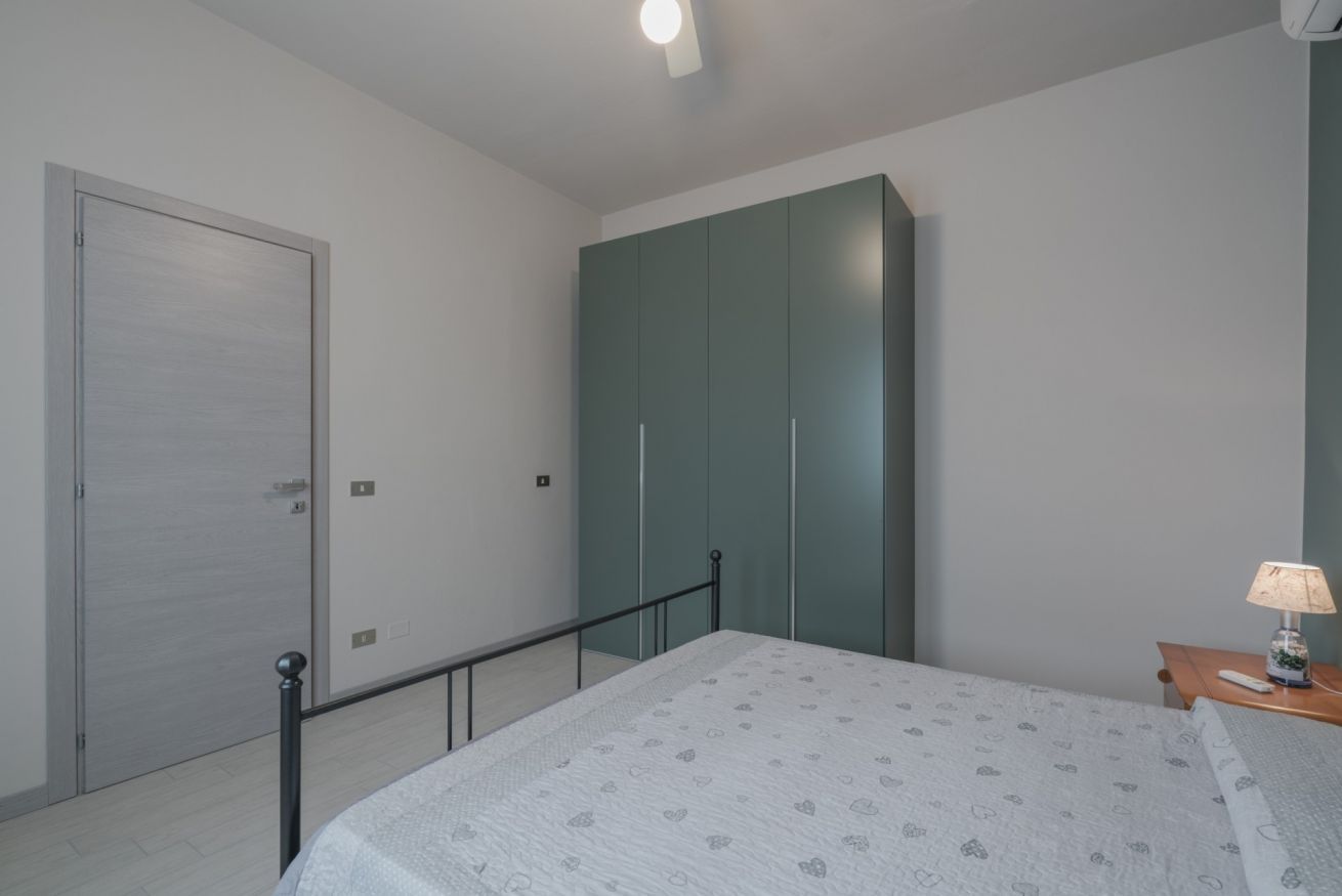 A bedroom with a bed, a wardrobe, a door, and a nightstand with a lamp.