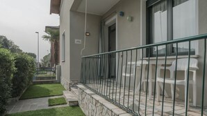A balcony with a stone wall, a metal railing, and white plastic chairs.
