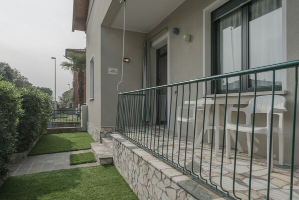 A balcony with a stone wall, a metal railing, and white plastic chairs.