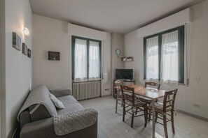 A modern living room with a sofa, a dining table with chairs, a TV, and a radiator. - Villa Natalina - Two-Bedroom Apartment with Air Conditioning and Wi-Fi (Sirmione)