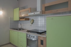 Eine Küche mit grünen Schränken, einem Edelstahlherd und einer gefliesten Spritzschutzwand.