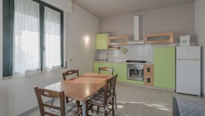 Una cocina compacta con una mesa y sillas, armarios verdes y un refrigerador blanco.