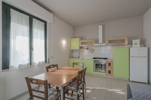 Una cocina compacta con una mesa y sillas, armarios verdes y un refrigerador blanco.