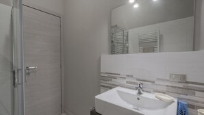 Un baño moderno con cabina de ducha de vidrio, un lavamanos blanco con un jabonera y un salpicadero de azulejos.