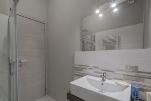 A modern bathroom with a glass shower enclosure, a white sink with a soap dish, and a tiled backsplash.