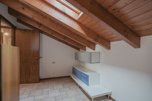 Een kamer met een schuine hemel, houten balken, een witte bank en een kledingkast.