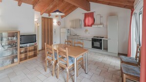 Une cuisine chaleureuse avec des poutres en bois, une table à manger avec des chaises, un téléviseur et un réfrigérateur.