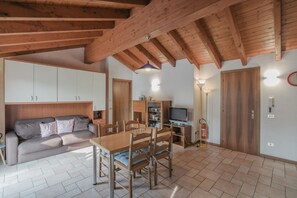Een gezellige woonkamer met houten plafond, een bank, een eettafel met stoelen en een televisie.