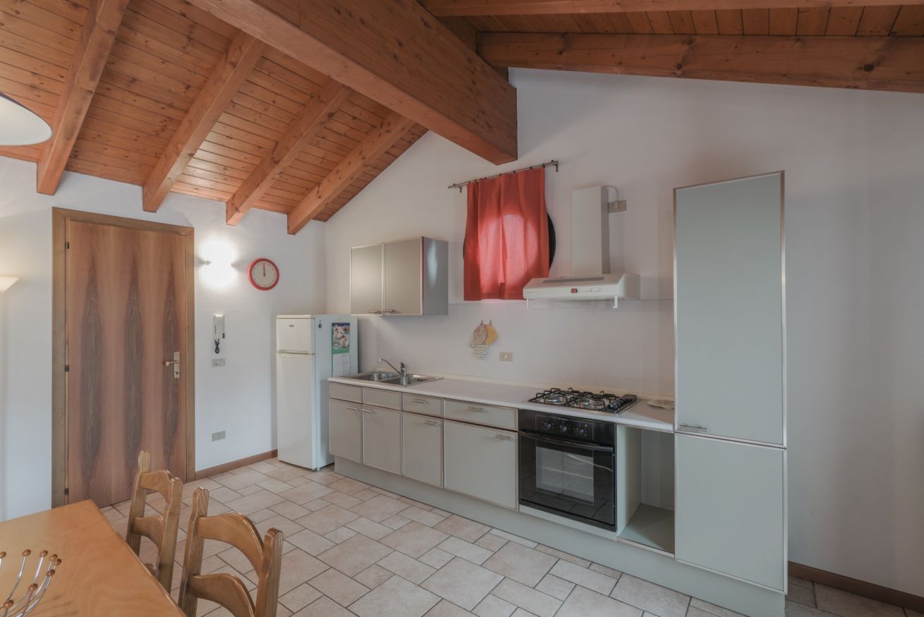 A kitchen with wooden beams, a stove, cabinets, a refrigerator, and a dining table with chairs.