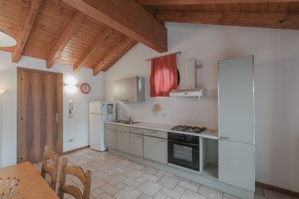 Een keuken met houten balken, een fornuis, kasten, een koelkast en een eettafel met stoelen.