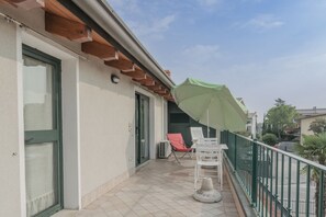 Un balcon avec un parasol vert, des chaises blanches et un sol carrelé.