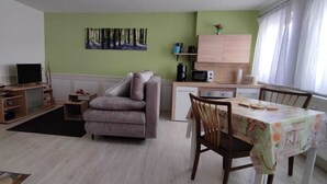 A compact living space with a sofa, a dining table, a kitchen area, and a TV.
