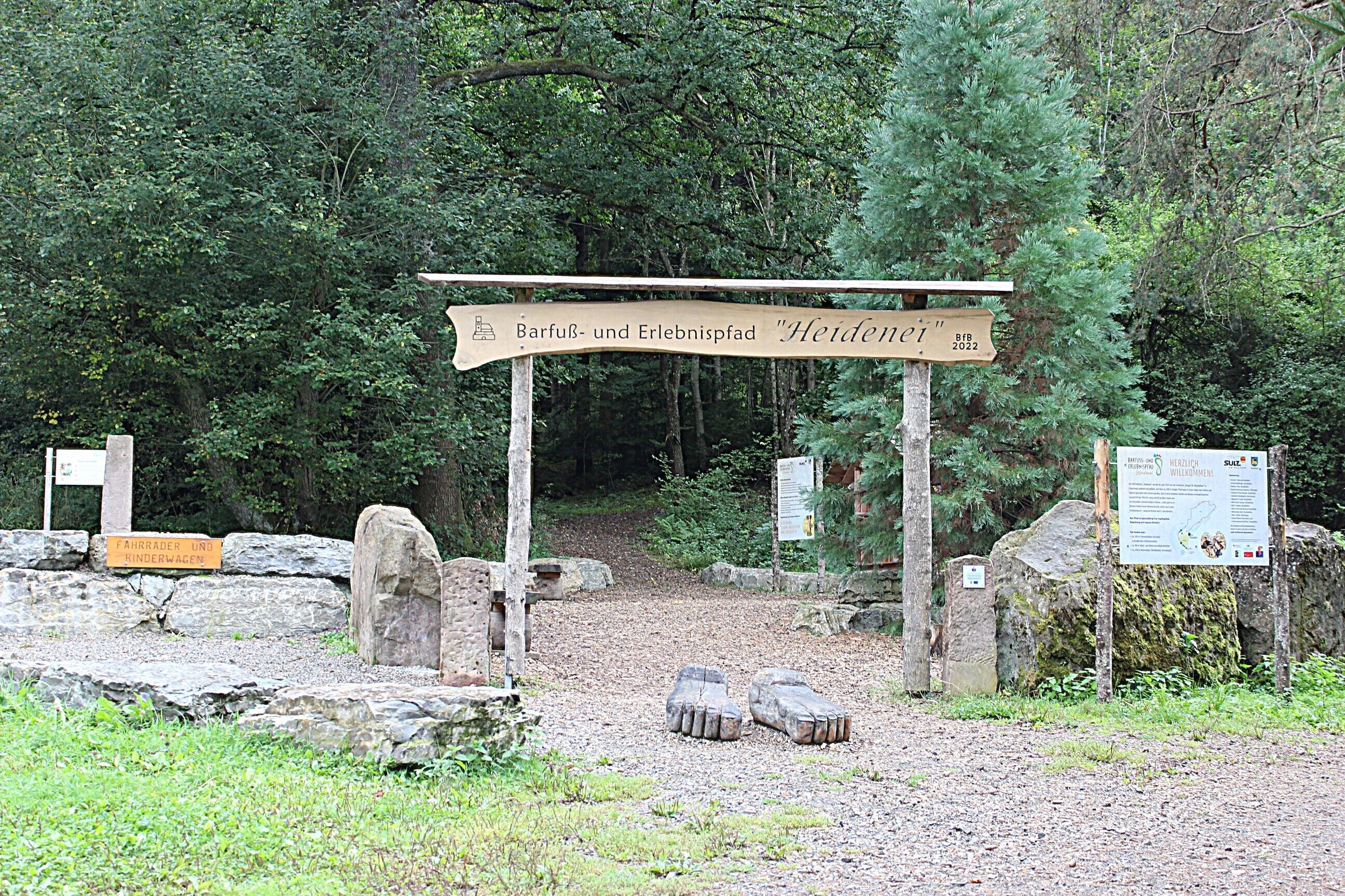 A wooden signpost with text, a stone pathway, and a forested area.