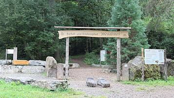 A wooden signpost with text, a stone pathway, and a forested area.