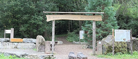 Un panneau indicateur en bois avec du texte, un sentier pavé de pierres et une zone boisée.