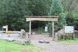 Un panneau indicateur en bois avec du texte, un sentier pavé de pierres et une zone boisée.
