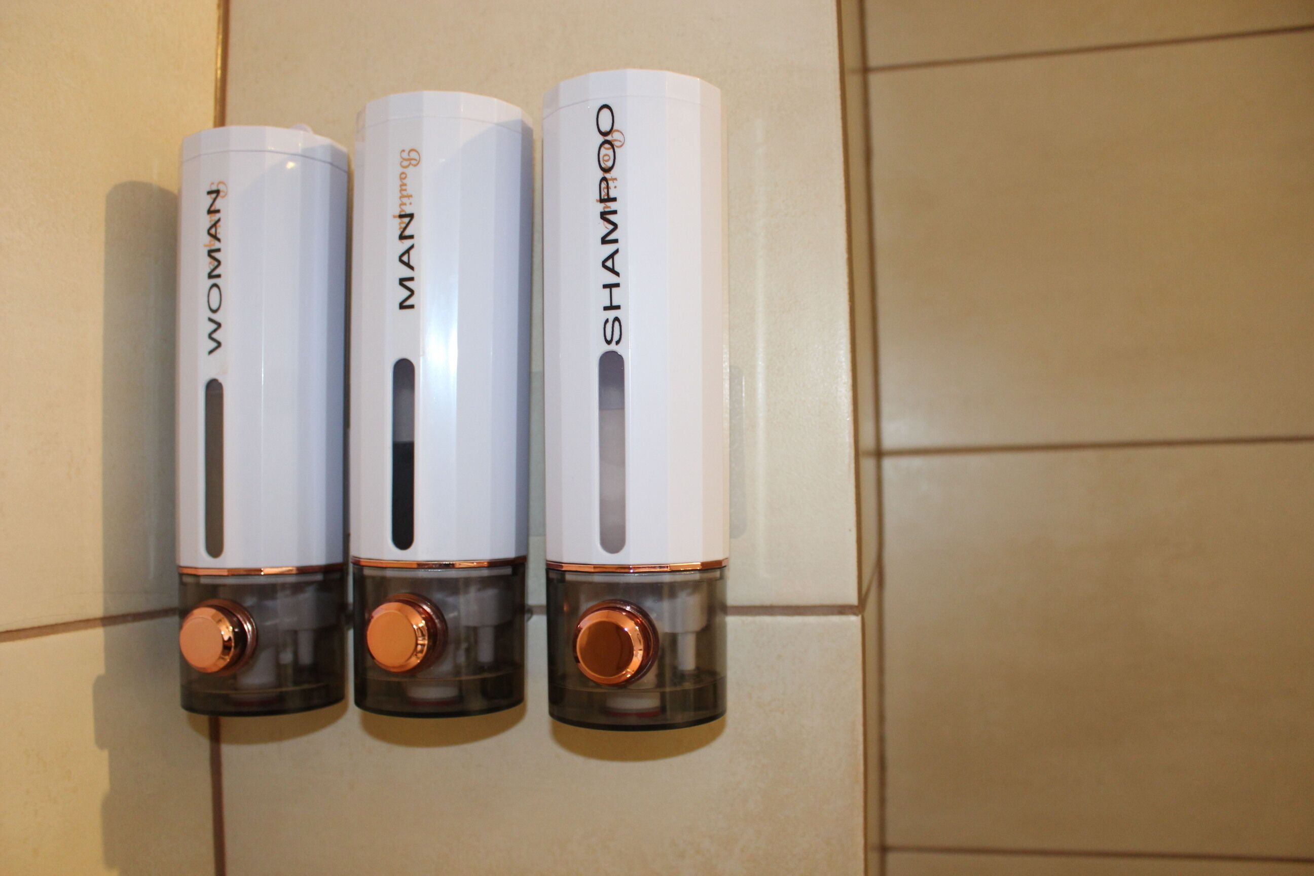 Trois bouteilles de shampoing sur un mur carrelé.