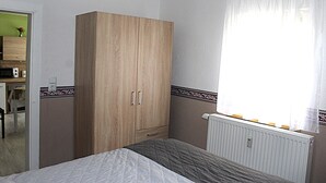 Un dormitorio con cama, armario, radiador y ventana con cortinas.