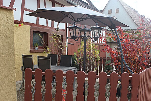 A patio with a table and chairs, a wooden fence, and a house with a sloped roof in the background.