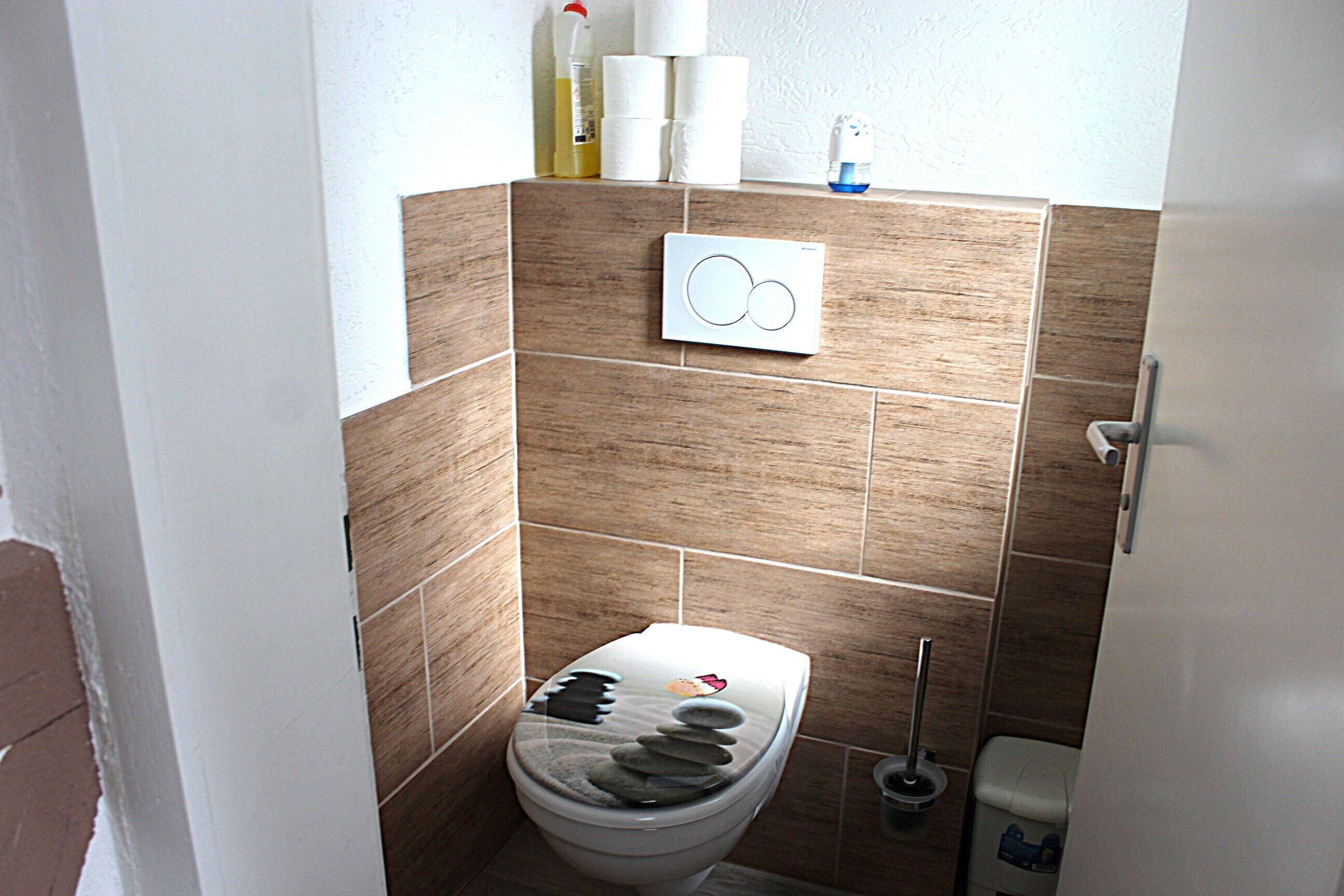 A bathroom with a toilet, a hand dryer, and a toilet brush.