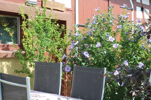 Ein Sitzbereich im Freien mit Tisch und Stühlen, umgeben von einem Garten mit violetten Blumen.